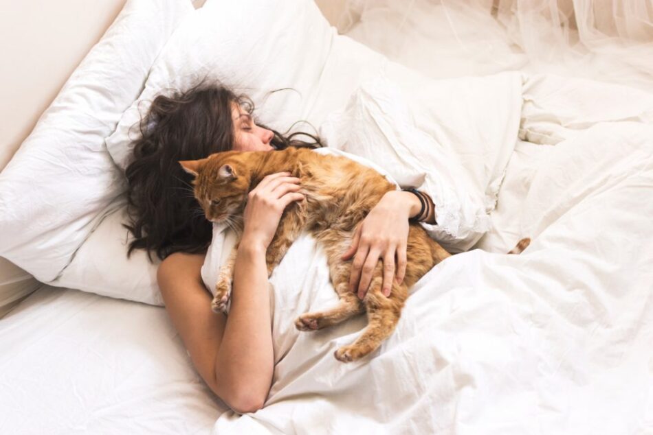 Woman asleep on bed, cuddling her cat