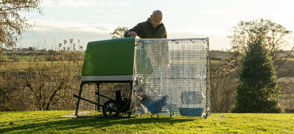 Man with his chickens in spring, using weather protection on the Omlet Eglu Go Up Chicken Coop