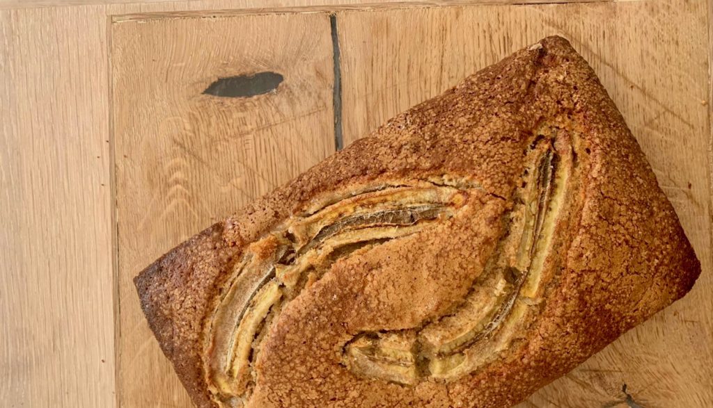 Et nybakt bananbrød, dekorert med en splittet banan som ligger på en trefjøl på kjøkkenbenken.