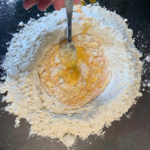 Hjemmelaget pasta: Tipo 00 melet ligger i en haug på kjøkkenbenken med innholdet av eggene i haugen i midten, halvveis blandet inn.