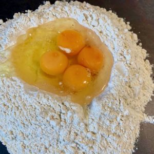 Hjemmelaget pasta: Tipo 00 melet ligger i en haug på kjøkkenbenken med innholdet av eggene i haugen i midten.