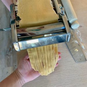 Hjemmelaget pasta: en hånd tar imot tagliatelle-pastaen som kommer ut av pastamaskinen. Nå trenger den bare å tørke, så kan den kokes eller fryses til når du selv måtte ønske å spise den!