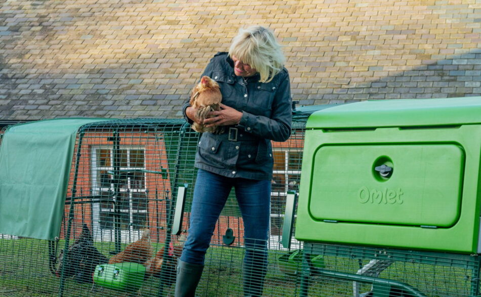 Woman holding chicken stepping out of Eglu Pro chicken coop run