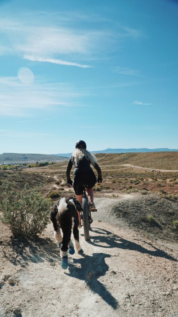 a woman on bike with her dog chasing behind 