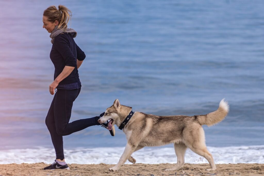 A woman jogging on a beach with her dog