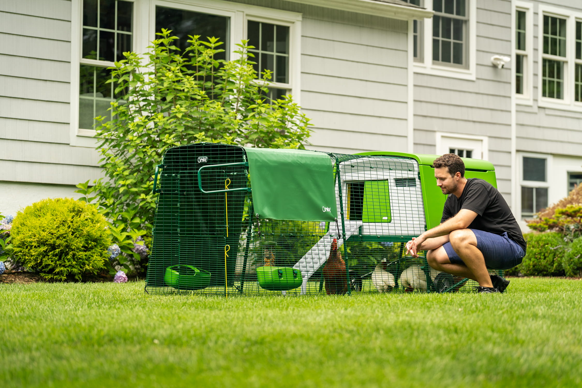 man kneeling next to eglu cube chicken coop with run in front of a house